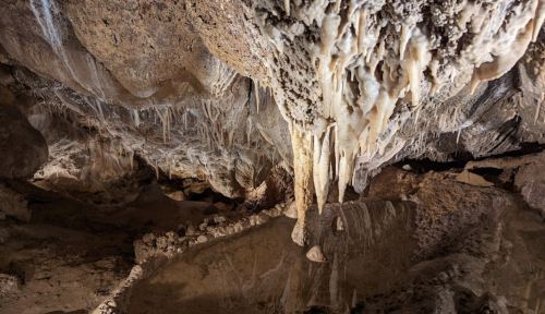 Stalactites and stalagmites in a dimly lit cave, with reflections in a shallow pool of water below.