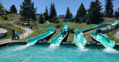 A water park featuring multiple turquoise water slides and a clear blue pool under a sunny sky.