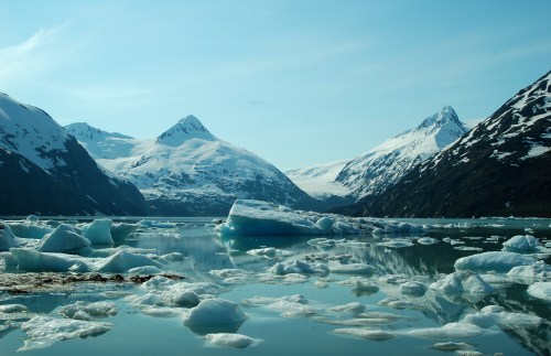 A serene glacial landscape with icebergs floating in calm waters, surrounded by snow-capped mountains under a clear sky.