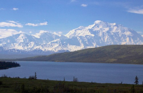 A serene landscape featuring a calm lake in the foreground and majestic snow-capped mountains in the background.