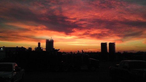 Silhouetted industrial structures against a vibrant sunset with orange and purple hues in the sky.