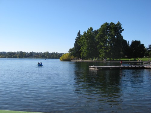 A serene lake scene with two people in a boat, surrounded by trees and a clear blue sky.
