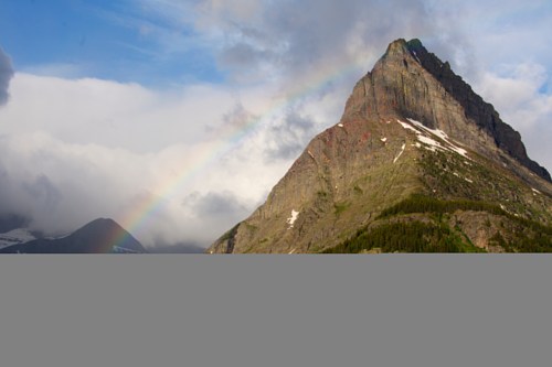 A majestic mountain peak under a cloudy sky, with a vibrant rainbow arching across the scene.