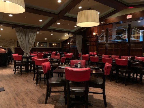 Interior of a restaurant featuring red chairs, wooden tables, and warm lighting, with a cozy, inviting atmosphere.