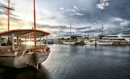 A serene marina scene at sunset, featuring boats docked in calm waters under a cloudy sky.