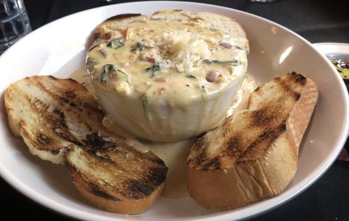 A bowl of creamy seafood chowder surrounded by toasted bread slices on a white plate.