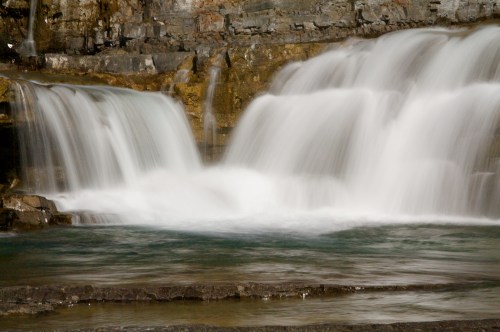 A serene waterfall cascading over rocks into a calm pool, surrounded by natural stone formations.