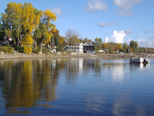 A serene lakeside view with colorful autumn trees, a calm water surface, and a boat near the shore.