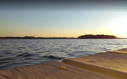 A serene view of a lake at sunset, with gentle waves and a distant island silhouetted against the colorful sky.