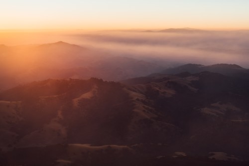 A serene landscape at sunset, with rolling hills shrouded in mist and a warm orange glow in the sky.