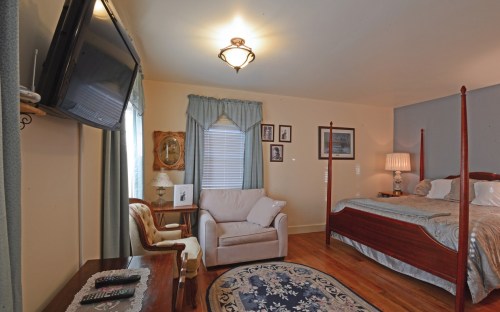 Cozy bedroom featuring a four-poster bed, armchair, TV, and decorative artwork on the walls. Warm, inviting atmosphere.