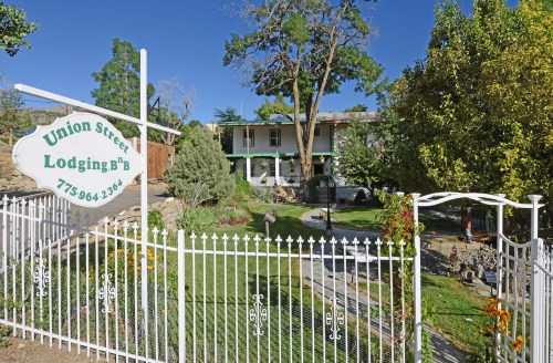 A charming bed and breakfast with a white picket fence, lush greenery, and a welcoming sign in a sunny outdoor setting.