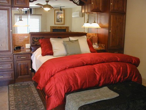 Cozy bedroom featuring a large red comforter, wooden cabinetry, and soft lighting.
