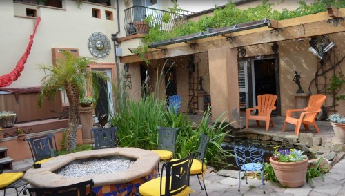 A cozy outdoor patio with colorful chairs, a stone fire pit, and lush greenery, creating a welcoming atmosphere.