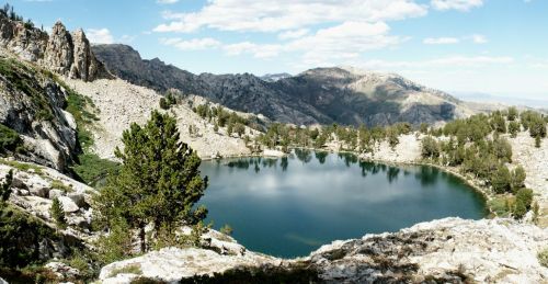 A serene mountain landscape featuring a calm lake surrounded by rocky terrain and lush greenery under a blue sky.