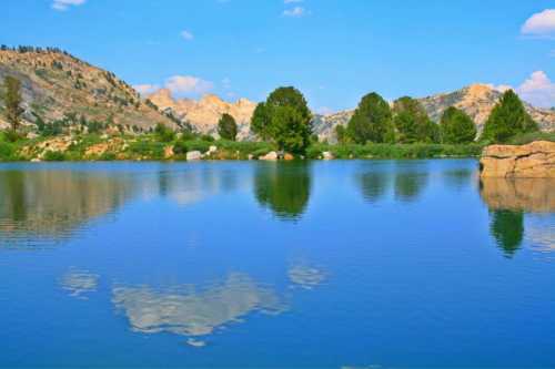 A serene lake reflecting mountains and trees under a clear blue sky.