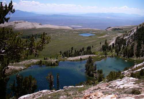 A scenic view of two blue lakes surrounded by green meadows and distant mountains under a clear sky.