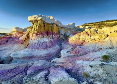 Colorful rock formations with layers of purple, yellow, and white under a clear blue sky.
