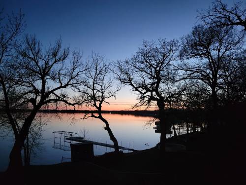 Silhouetted trees frame a tranquil lake at dusk, with a gradient sky transitioning from blue to orange.