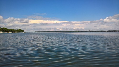 A serene lake scene with gentle waves, under a bright blue sky and fluffy white clouds.