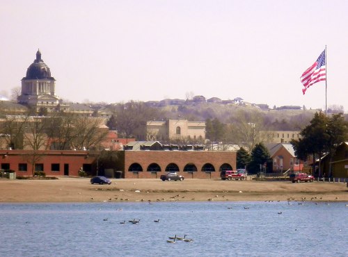 View of a lake with ducks, a large American flag, and a historic building with a dome in the background.