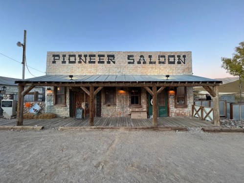 A rustic building labeled "Pioneer Saloon" with a wooden porch, set against a clear sky.