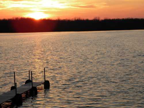 A serene sunset over a calm lake, with a wooden dock extending into the water.