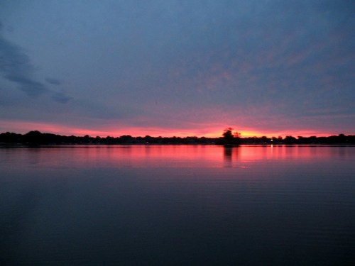 A serene lake at sunset, reflecting vibrant pink and orange hues against a cloudy sky.