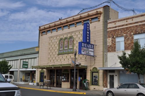 Historic theater building with decorative facade and marquee, located on a street with a liquor store nearby.