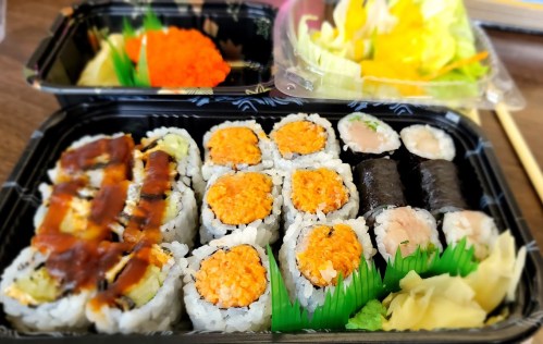 A sushi platter featuring various rolls, including salmon and eel, with wasabi, ginger, and a side salad.