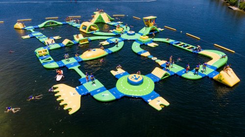 Aerial view of a colorful inflatable water park with various slides and obstacles on a lake, filled with people enjoying.