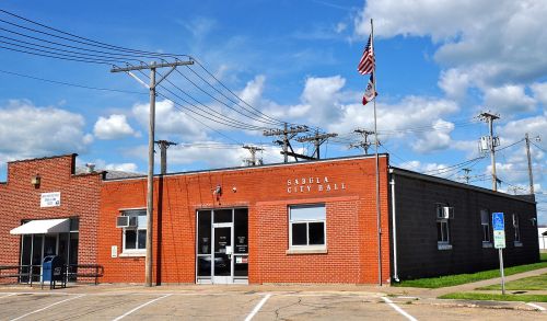 A brick building labeled "Sabula City Hall" with an American flag, surrounded by power lines and a clear blue sky.