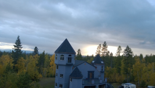A gray castle-like building surrounded by trees with autumn foliage under a cloudy sky.