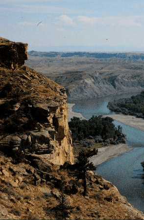 A scenic view of a river winding through rugged terrain, with cliffs and sparse vegetation under a clear sky.