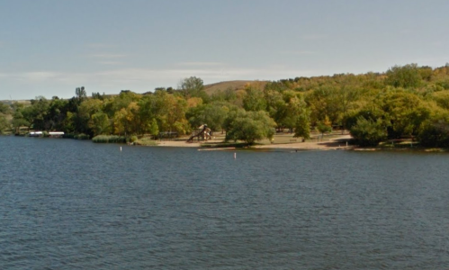 A serene lake view with a sandy beach and trees lining the shore under a clear sky.