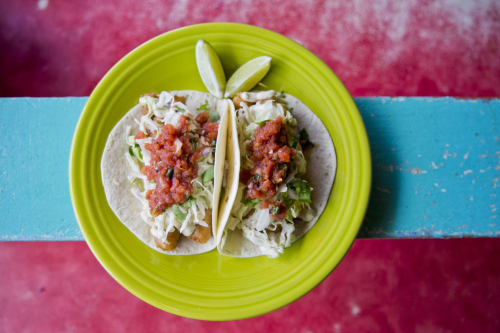 Two tacos on a bright green plate, topped with lettuce, salsa, and lime wedges, resting on a colorful table.