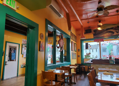 Colorful restaurant interior with green trim, wooden tables, and vibrant decor, featuring an exit door and large windows.