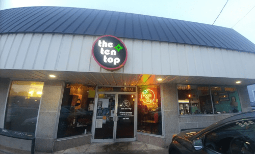 Exterior of a restaurant called "The Ten Top," featuring a sign and large windows, with a car parked in front.