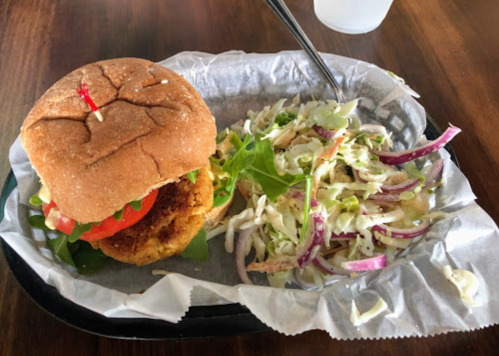 A crispy chicken sandwich with lettuce, tomato, and a side of coleslaw on a tray.