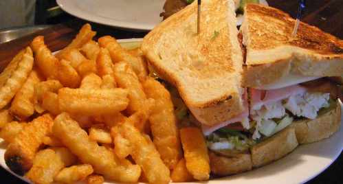 A toasted sandwich with layers of meat and vegetables, served with a side of crispy crinkle-cut fries.