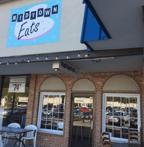 Exterior of Midtown Eats restaurant with a blue sign and arched windows, featuring outdoor seating and an "Open" sign.