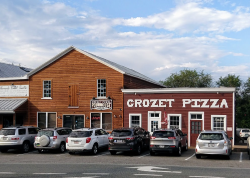 A rustic building with a sign for Crozet Pizza and a nearby establishment called "Pourhouse," surrounded by parked cars.