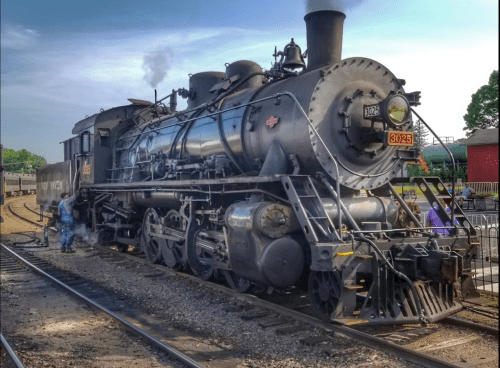 A vintage steam locomotive with a shiny black exterior, parked on tracks with workers nearby.