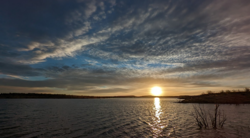 A serene sunset over a calm lake, with colorful clouds reflecting on the water's surface.