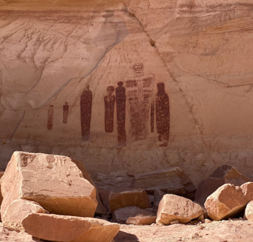Ancient rock art depicting human figures on a cliff face, surrounded by large boulders.