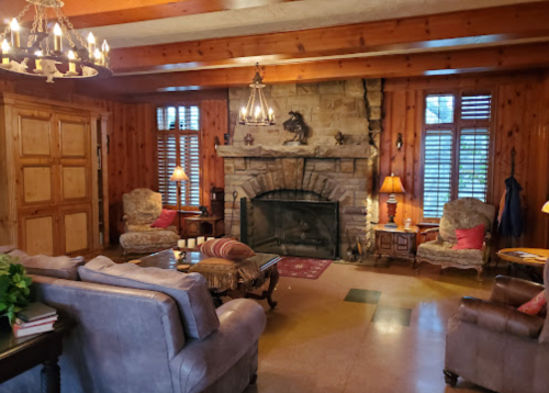 Cozy living room with wooden walls, stone fireplace, plush seating, and warm lighting.