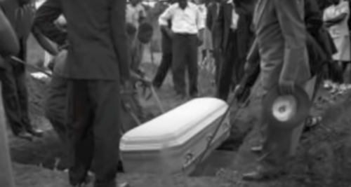 A group of people gathers around as a coffin is lowered into a grave during a burial ceremony.