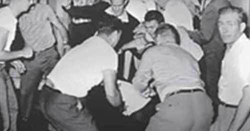 A group of people gathered around, assisting someone on the ground in a chaotic scene.
