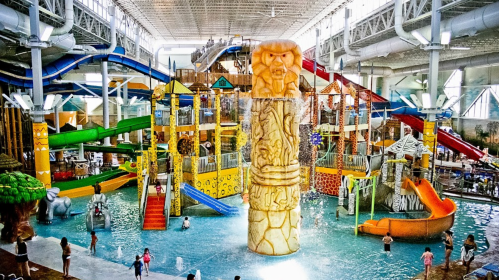 A vibrant indoor water park featuring slides, a large totem, and families enjoying the water attractions.