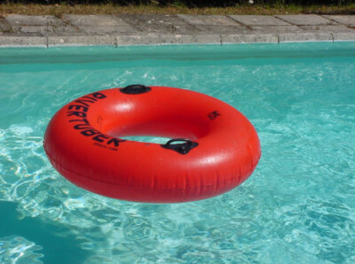 A bright red inflatable inner tube floating in a clear blue swimming pool.